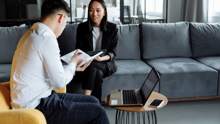 Two people collaborating working on a laptop and going over notes